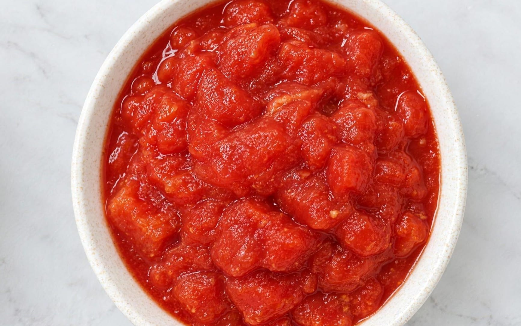 Chopped tomatoes seen from directly above: soft irregular chunks of peeled tomato packed in thick red juice.