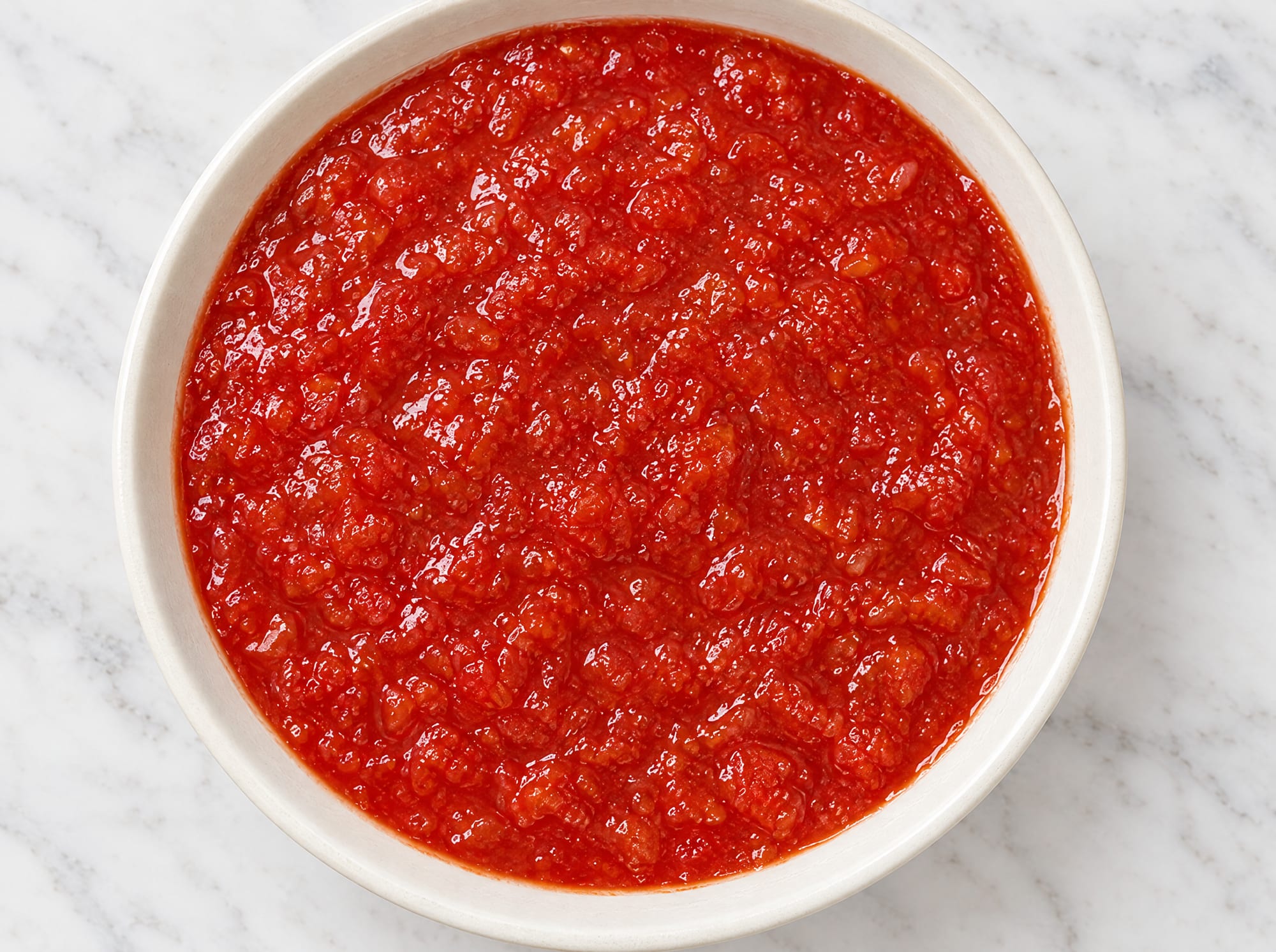 Looking straight down into a bowl of Mazza crushed tomatoes: a glossy deep red pulp of soft tomato pieces.