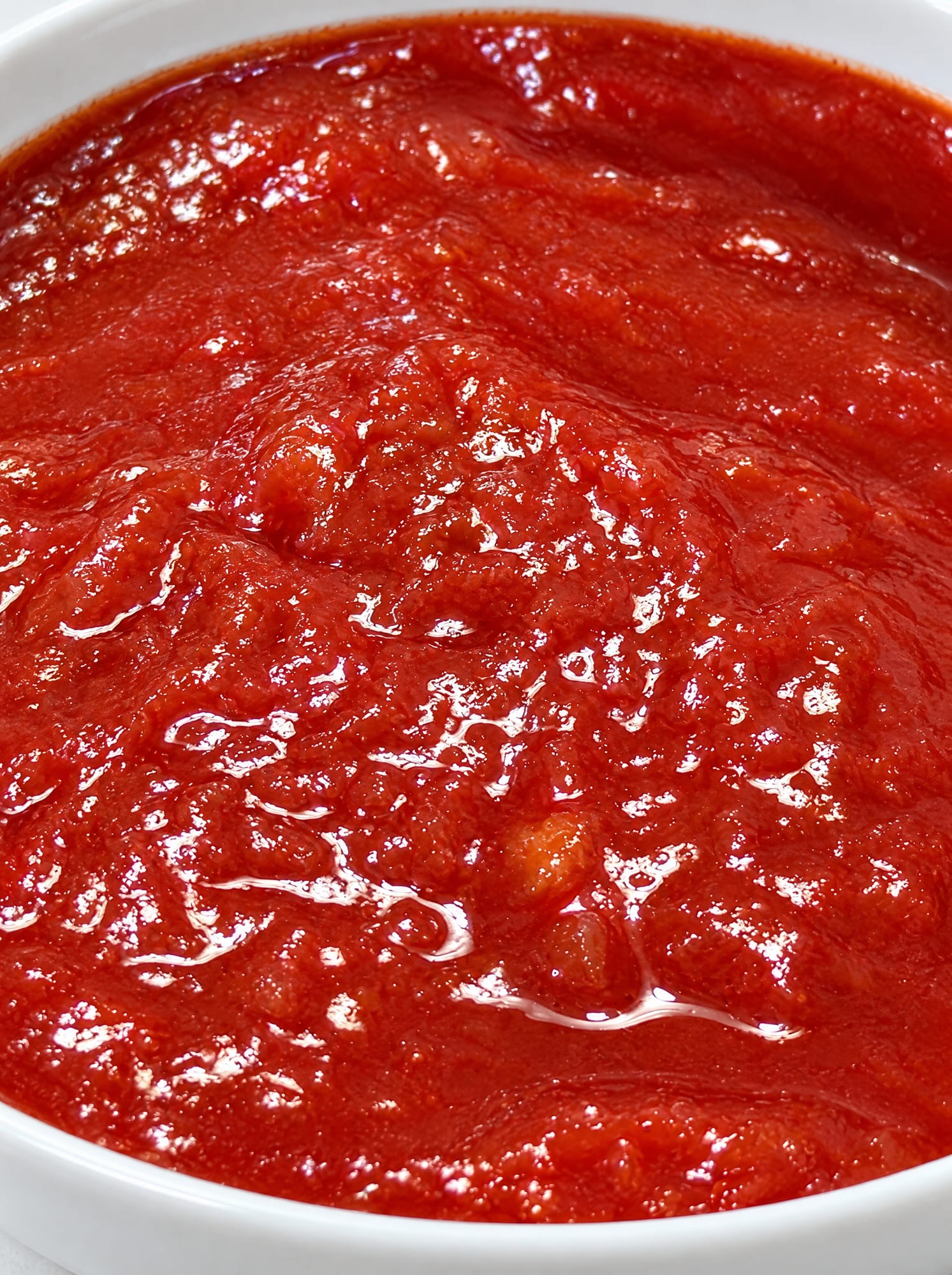 Close-up of crushed tomatoes: soft fragments of tomato in a thick, glossy red pulp.