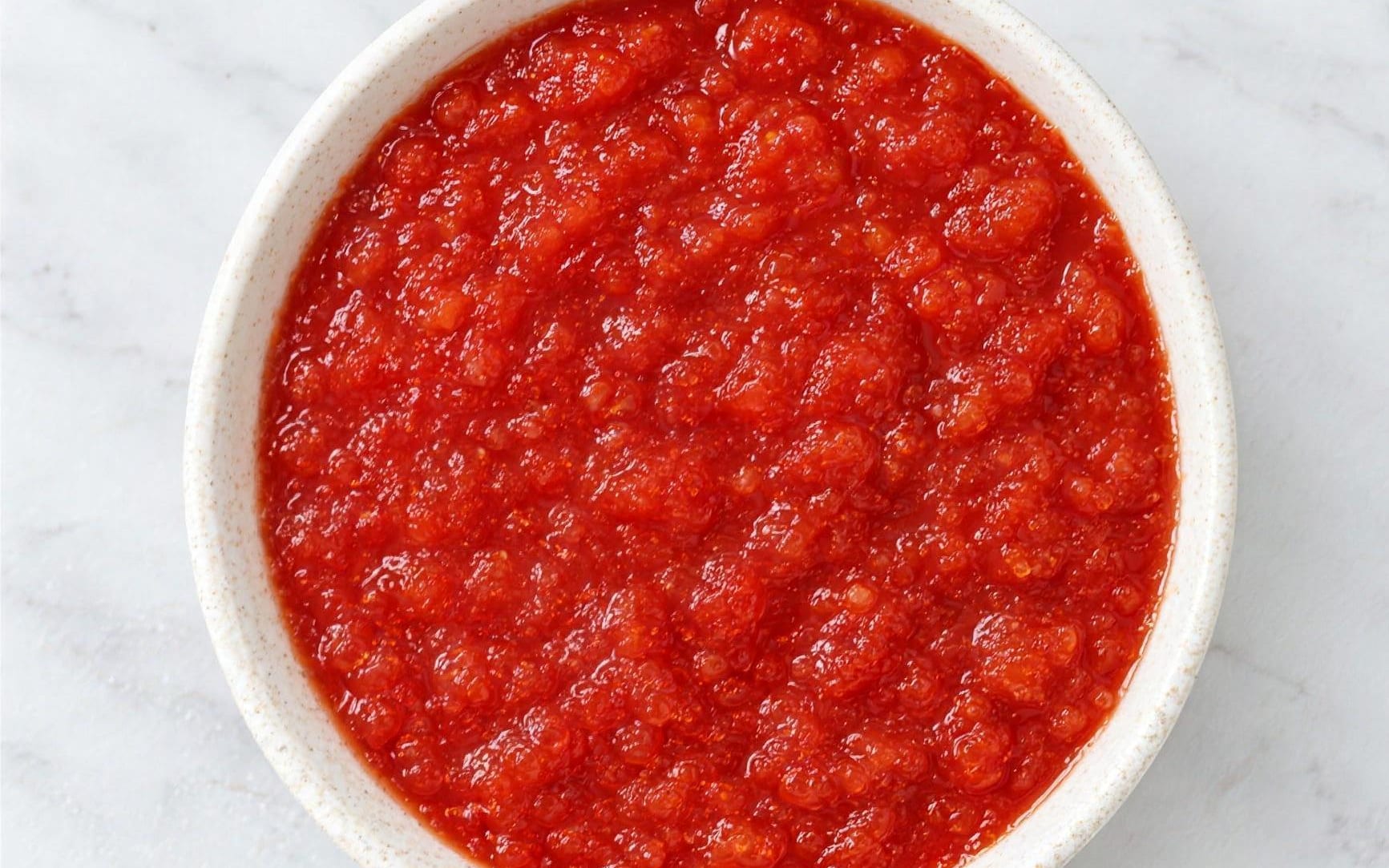 Crushed tomatoes seen from directly above: a dense pulp of small soft fragments in thick red juice.