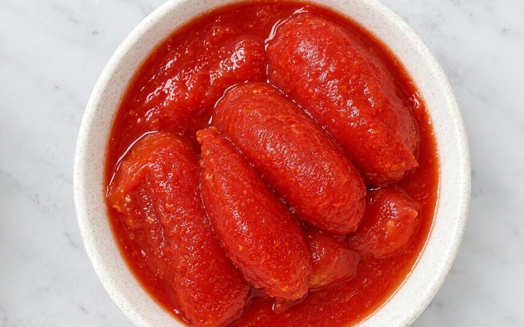 Whole peeled plum tomatoes seen from directly above, lying intact in a loose red juice.